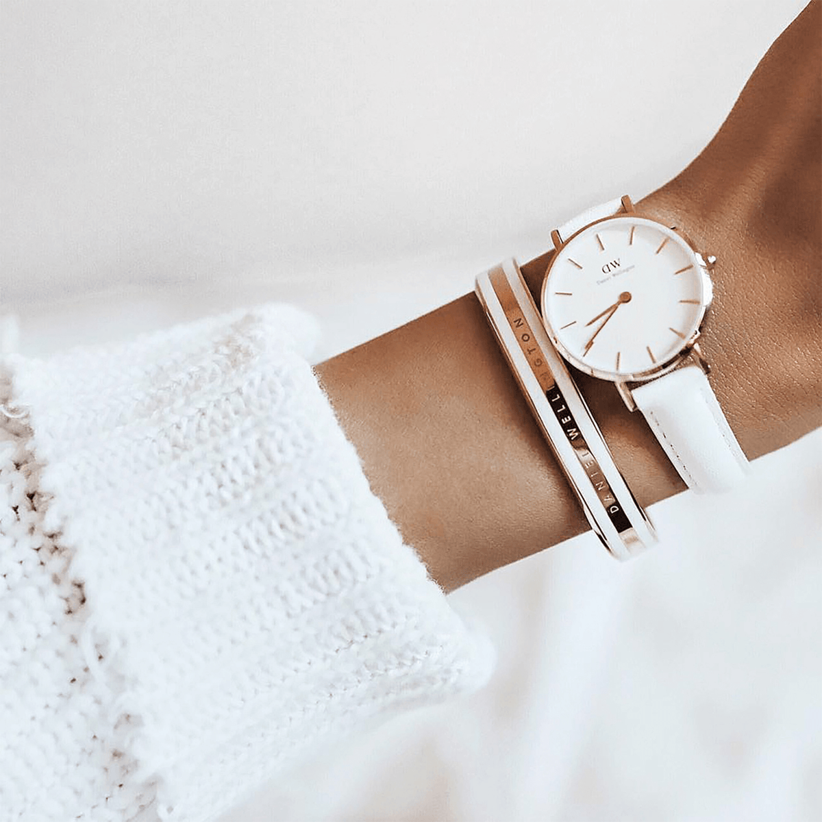 The Emalie Bracelet Satin White Rose Gold is styled on the wrist next to a white Daniel Wellington watch, highlighting its satin white enamel and rose gold finish for a coordinated, elegant look.