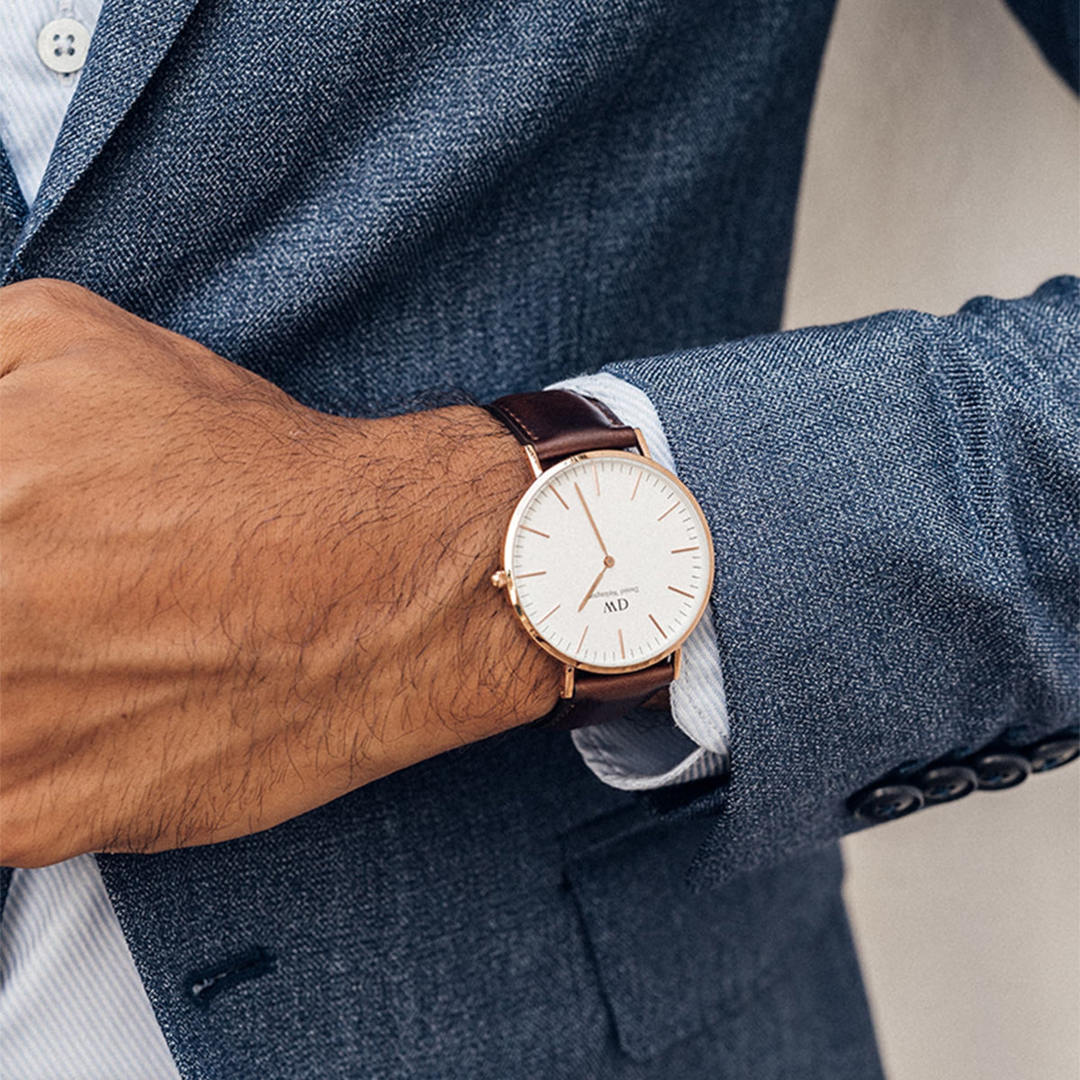 A man wearing the Classic Bristol Rose Gold watch with a white dial and dark brown leather strap, styled with a blue suit jacket for a smart, elegant look.