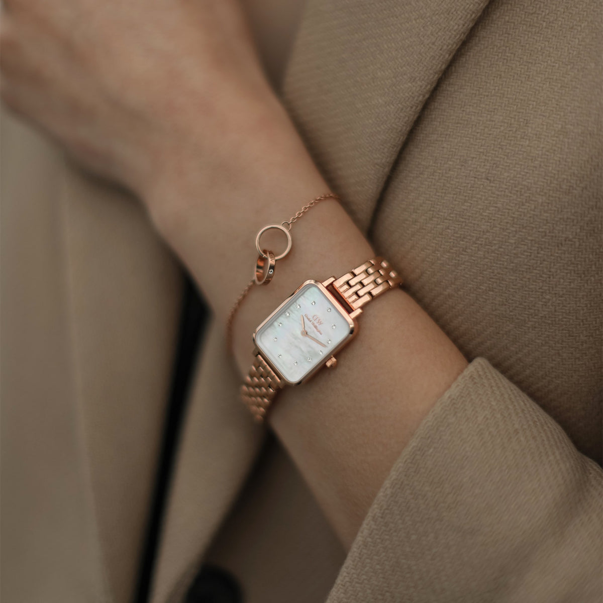 Quadro Lumine 5 Link Melrose White MoP Rose Gold women’s watch with a rectangular rose gold case and white mother of pearl dial, styled on the wrist with a matching rose gold bracelet and a beige coat.