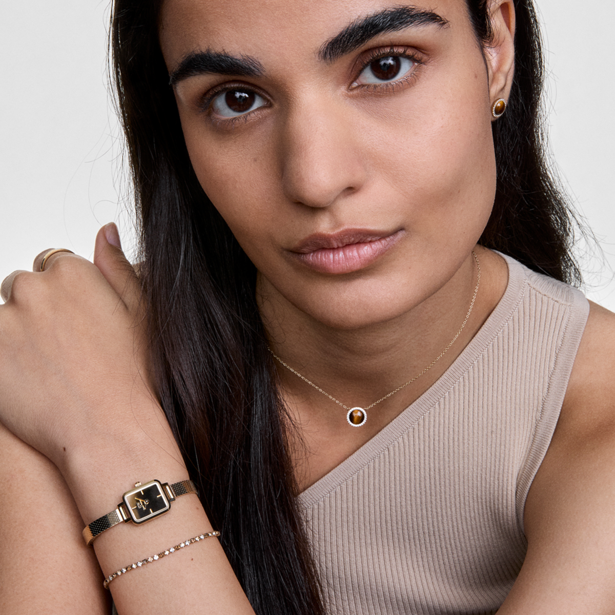 Woman wearing the Honey Gold Set by Daniel Wellington, featuring a gold mesh strap watch with a square face, a sparkling tennis bracelet, and a delicate gold necklace with a honey-toned pendant, styled together for an elegant and contemporary look.