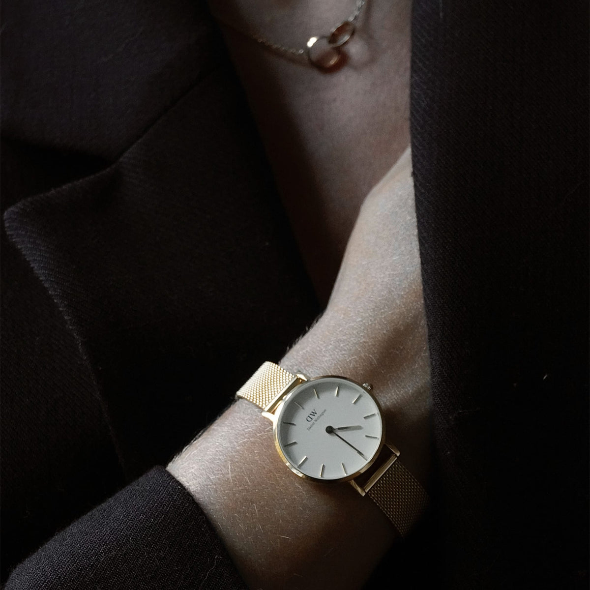 Woman wearing Petite Evergold gold mesh watch with white dial, styled with a dark blazer and delicate necklace.