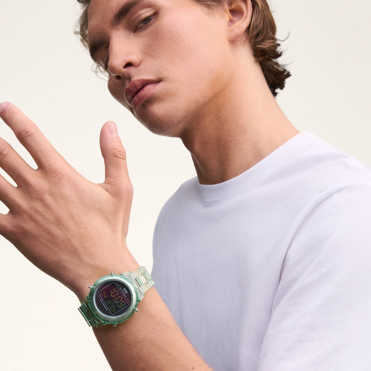 A man wearing the Daniel Wellington Retro Digital Light Green watch, featuring a transparent light green strap and round black digital dial, styled with a plain white t-shirt.