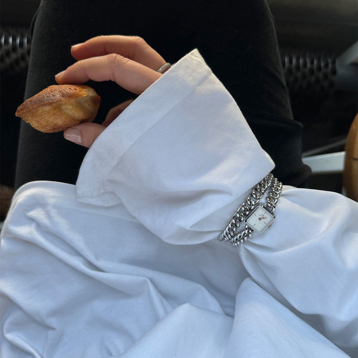 Woman wearing Jolie & Chunky Chain Silver Set watch and bracelet with white shirt, holding a pastry.