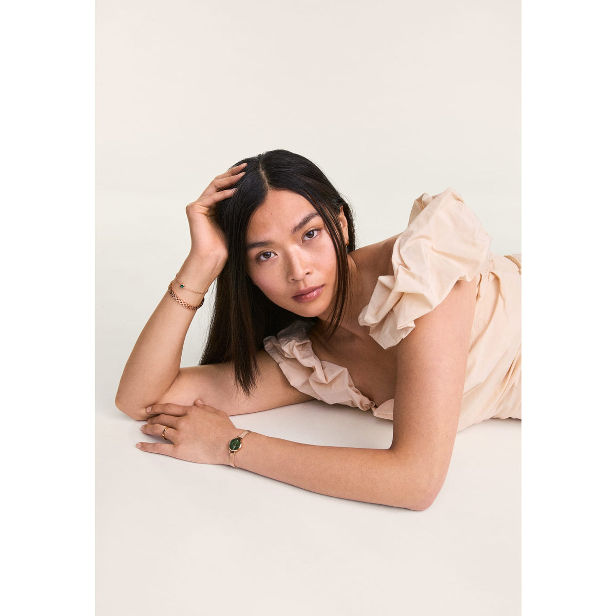 Woman wearing the Petite Mini Emerald Melrose watch with an emerald green dial and rose gold mesh strap, styled with a soft cream ruffle dress for an elegant, feminine look.