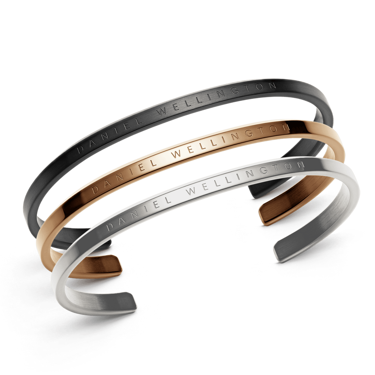 Set of three Daniel Wellington cuff bracelets in black, rose gold, and silver stainless steel, each featuring a minimalist open design with the brand name elegantly engraved along the band.