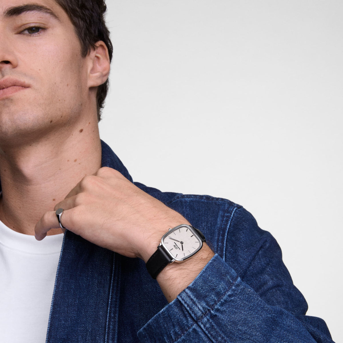 Marlon Sheffield Linen Silver men’s watch with silver cushion case, beige dial, and black leather strap styled with denim.