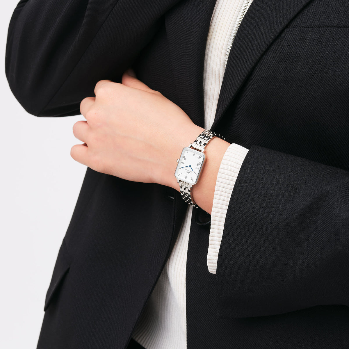 Woman wearing Quadro Roman Numerals 5-Link Silver watch with blue hands and rectangular dial, styled with a black blazer.