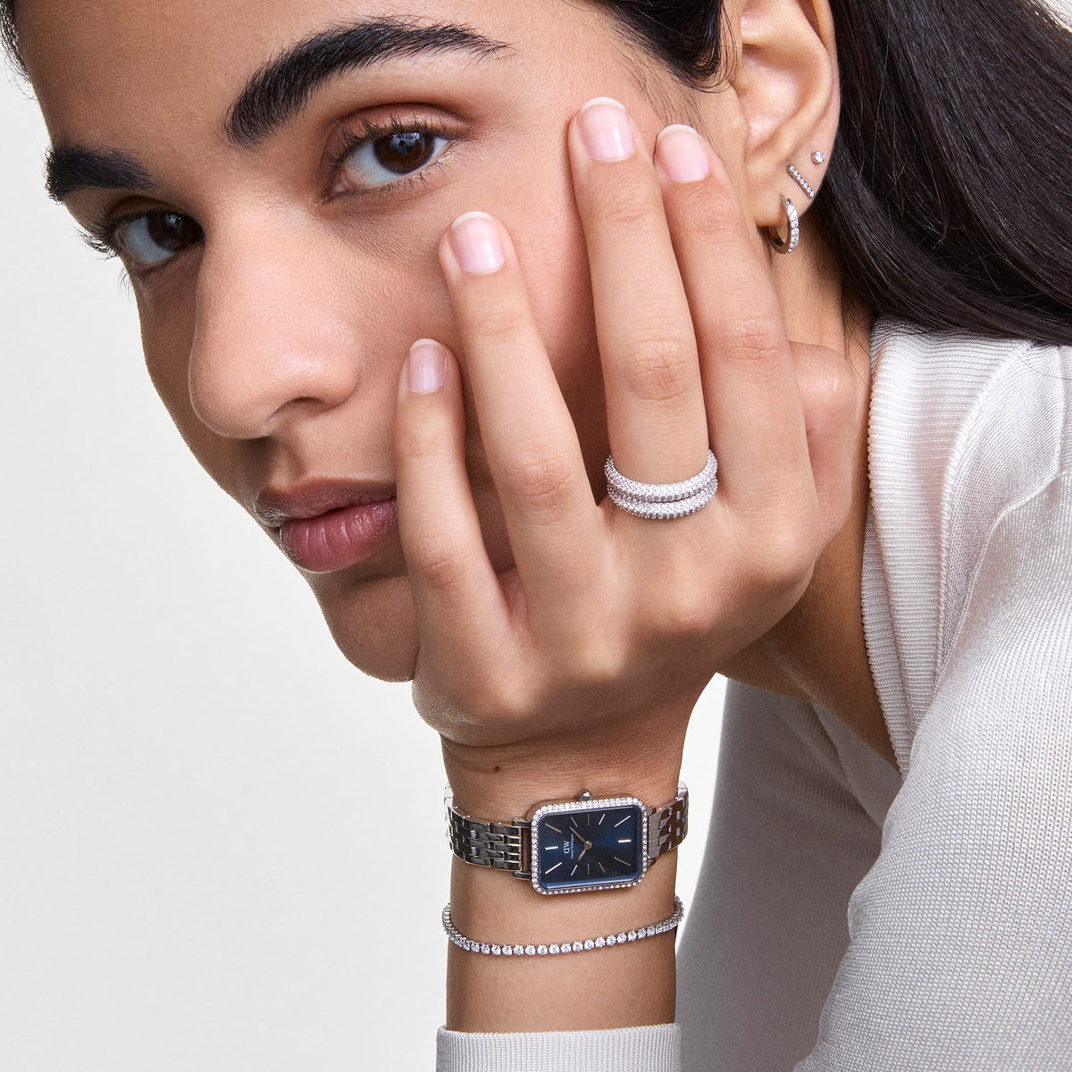 Woman wearing the Classic Tennis Bracelet Silver on her wrist, styled with a silver watch and matching jewellery, showcasing the bracelet’s row of sparkling cubic zirconia crystals and elegant, polished finish.