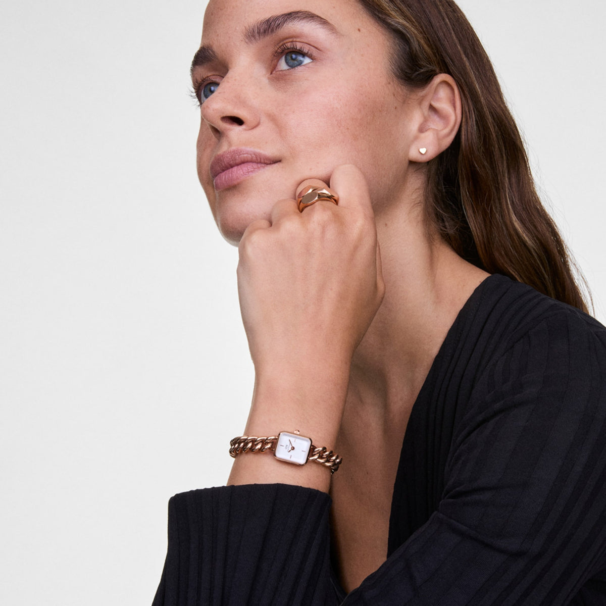 Woman wearing the Jolie Chain Rose Gold watch, featuring a square white dial and a chunky rose gold chain bracelet, styled with a black top and matching rose gold jewellery for a sophisticated look.
