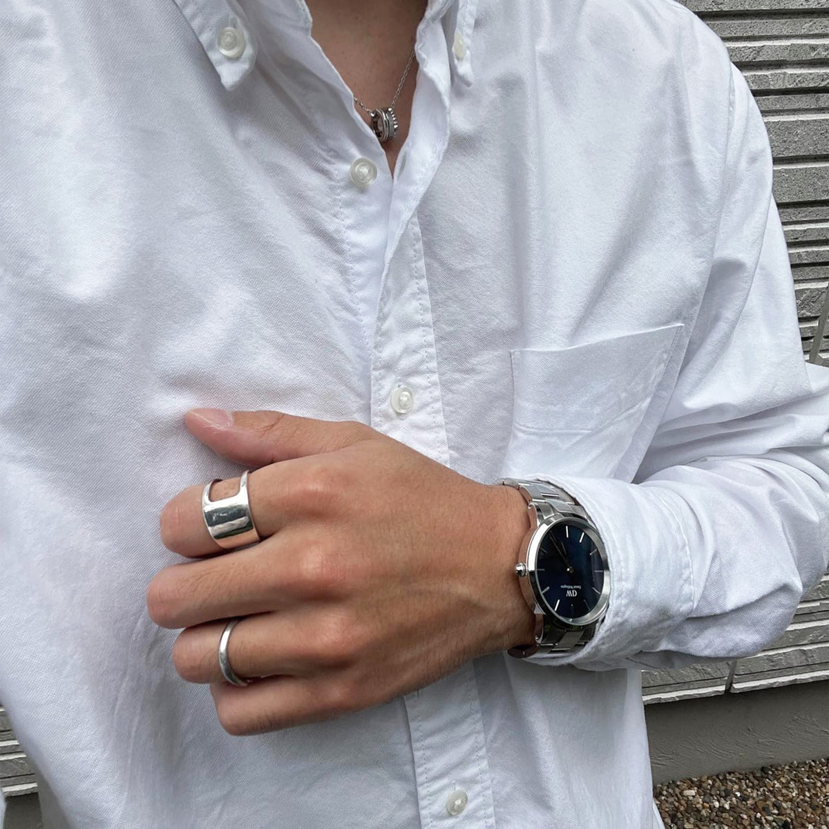 Daniel Wellington Iconic Link Silver watch with black dial and stainless steel strap, styled with a white shirt and silver rings.