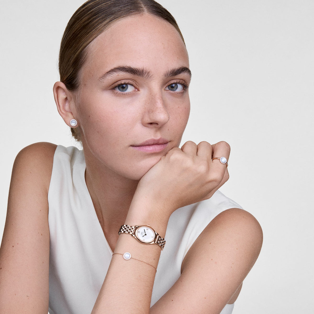 Woman wearing Audrey mother of pearl rose gold stud earrings, styled with matching bracelet, ring and watch for a chic look.