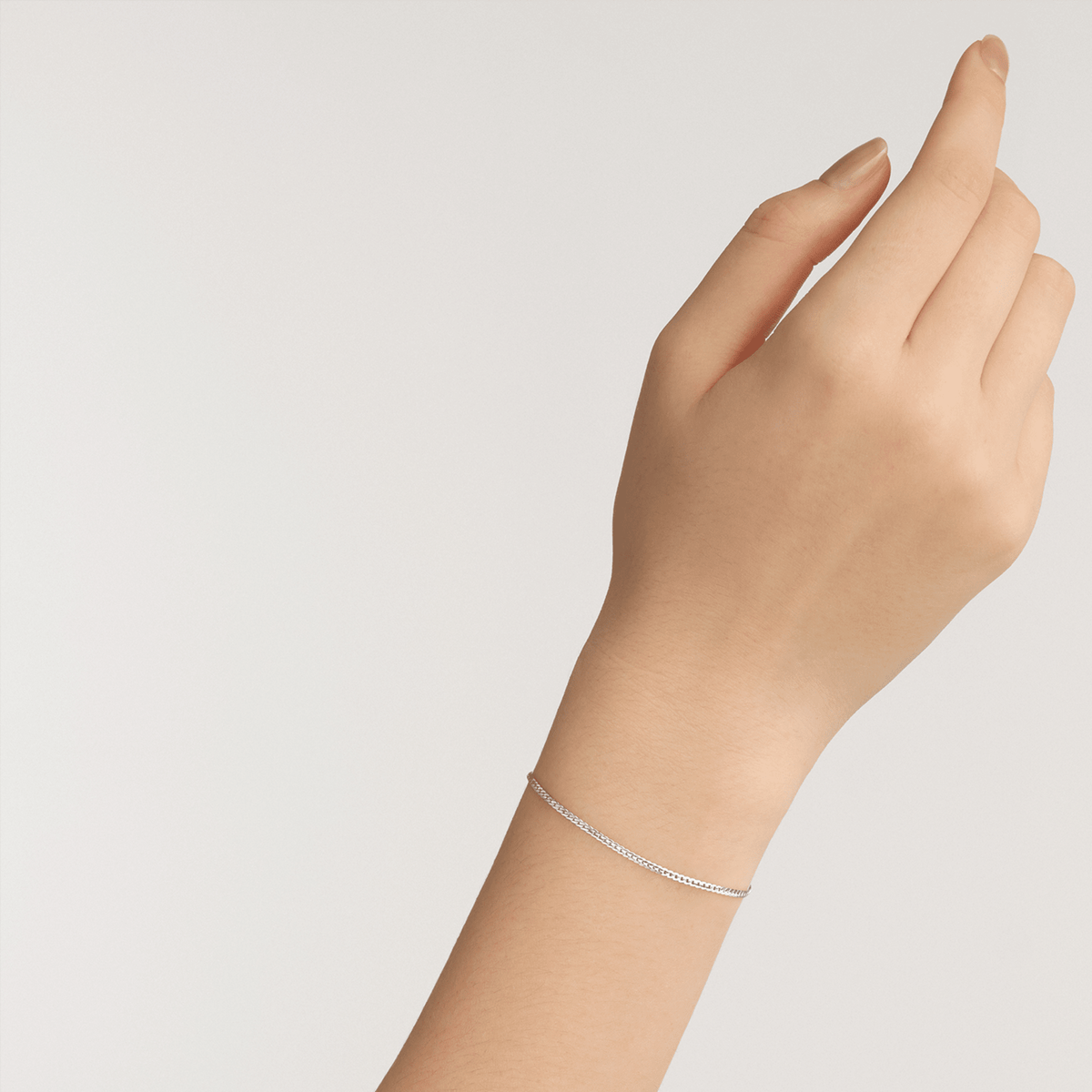 A delicate silver flat chain bracelet with a minimalist design is worn on the wrist, showcasing its slim and elegant style.
