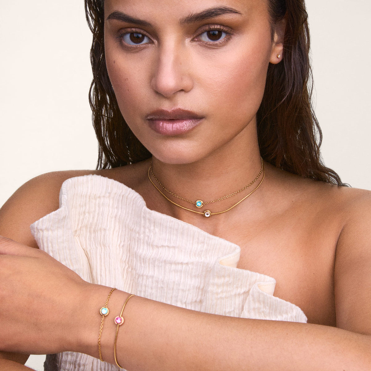 A woman wearing a gold bracelet featuring the October Charm S925 Sterling Silver with a pink opal crystal, styled alongside other delicate jewellery for an elegant, layered look.