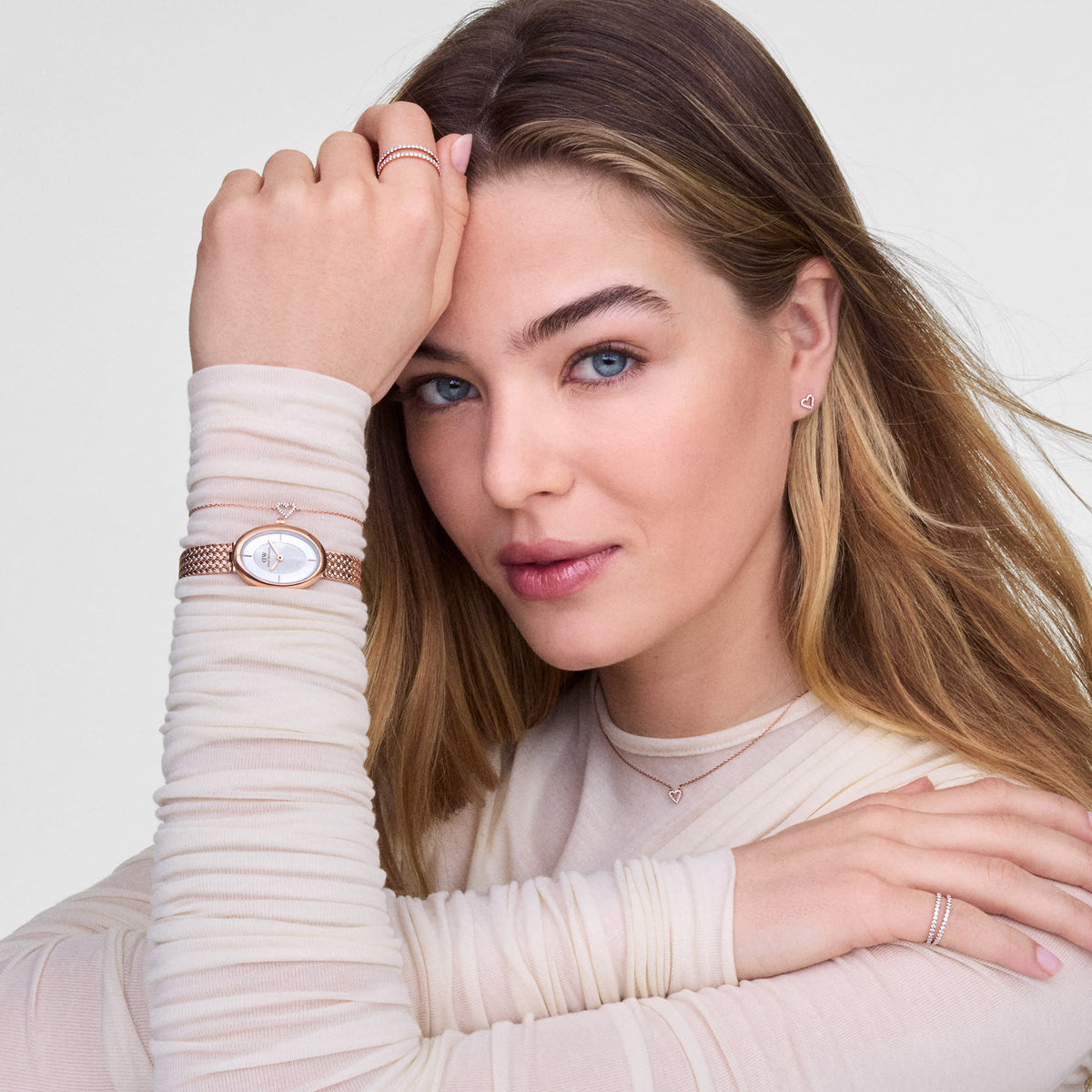 Woman wearing Mirelle Heart Earring Rose Gold studs, styled with matching rose gold jewellery including a watch, necklace, and rings, highlighting the delicate open-heart design and sparkling cubic zirconia detail.