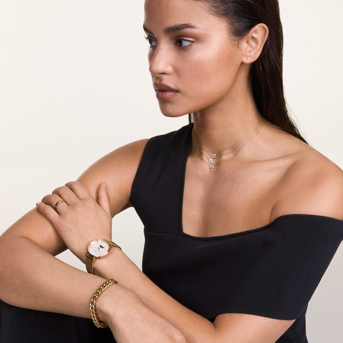 A woman wears the Crystal Zodiac Chain Necklace Silver with a sparkling Scorpio pendant, styled with a black off-shoulder top and gold accessories.
