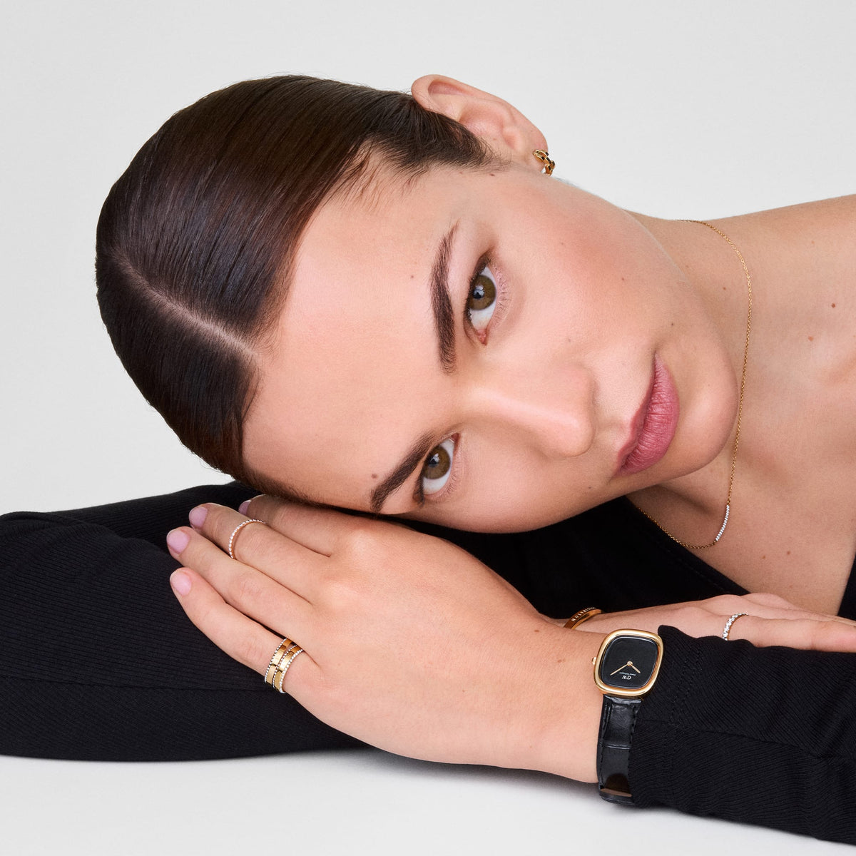 A woman wears the Mirelle Eternity Necklace Gold, featuring a fine gold chain with a row of white cubic zirconia crystals, styled elegantly with a black top and gold jewellery for a refined everyday look.