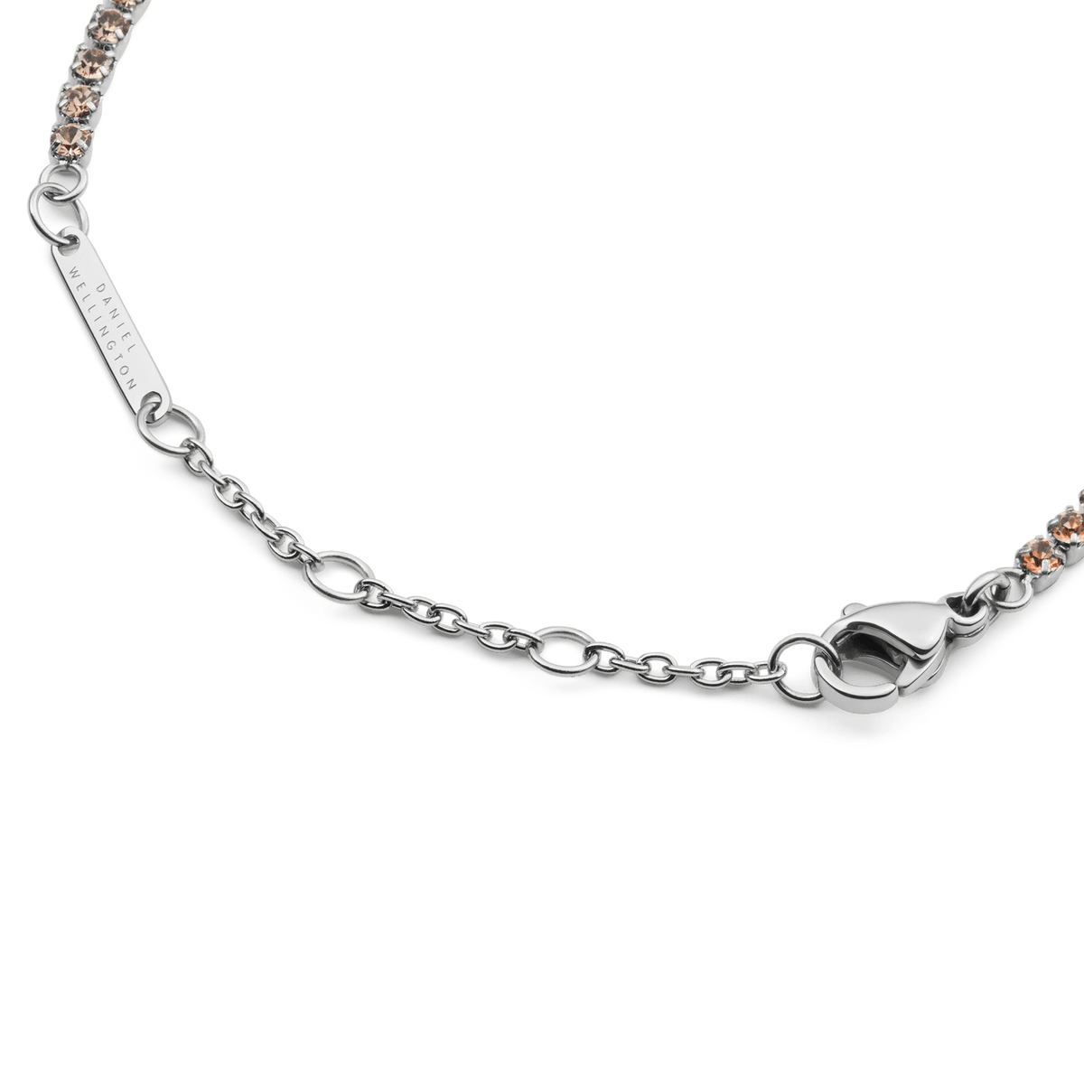 Detail view of the Classic Tennis Bracelet Apricot Silver, showing the adjustable silver chain, secure lobster clasp, and Daniel Wellington logo tag alongside apricot-coloured crystals.