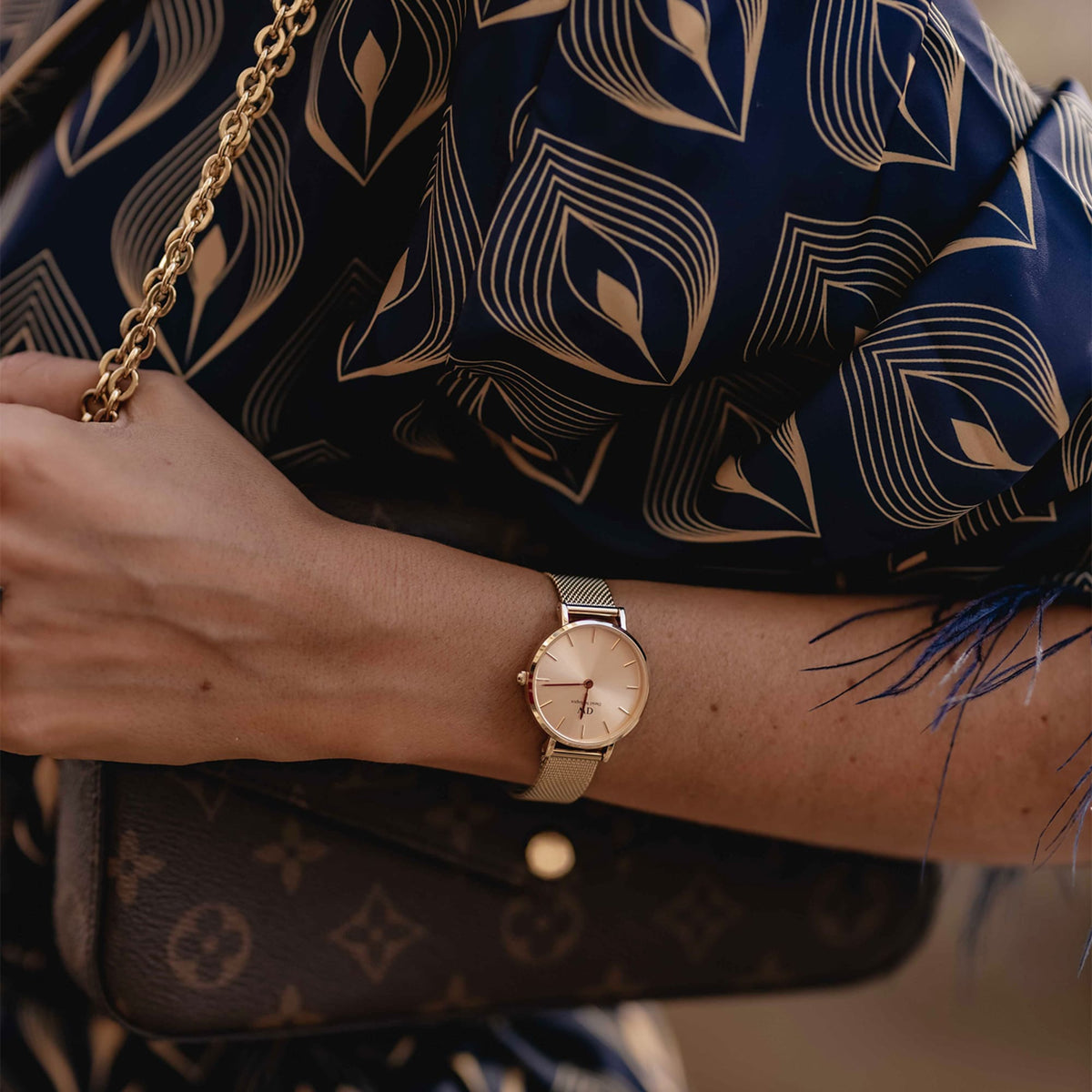 Woman wearing the Petite Unitone rose gold watch with a minimalist dial and mesh strap, styled with a patterned blouse and a designer handbag.