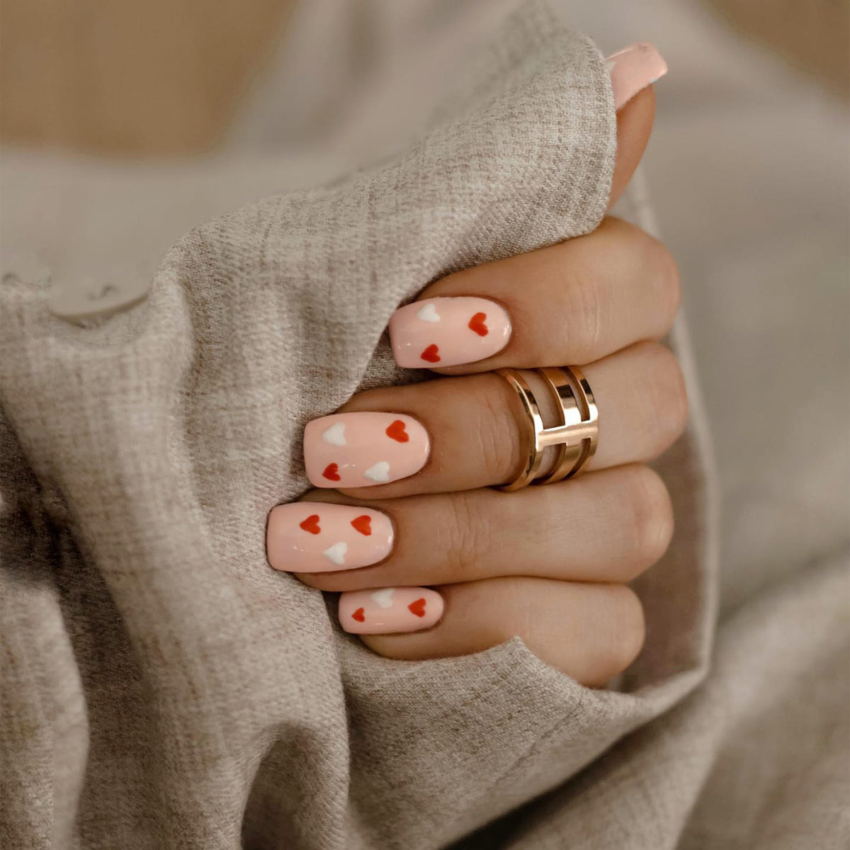 Elan Triad Ring Rose Gold worn on a hand with pink heart-patterned nails, showcasing its elegant three-band design.