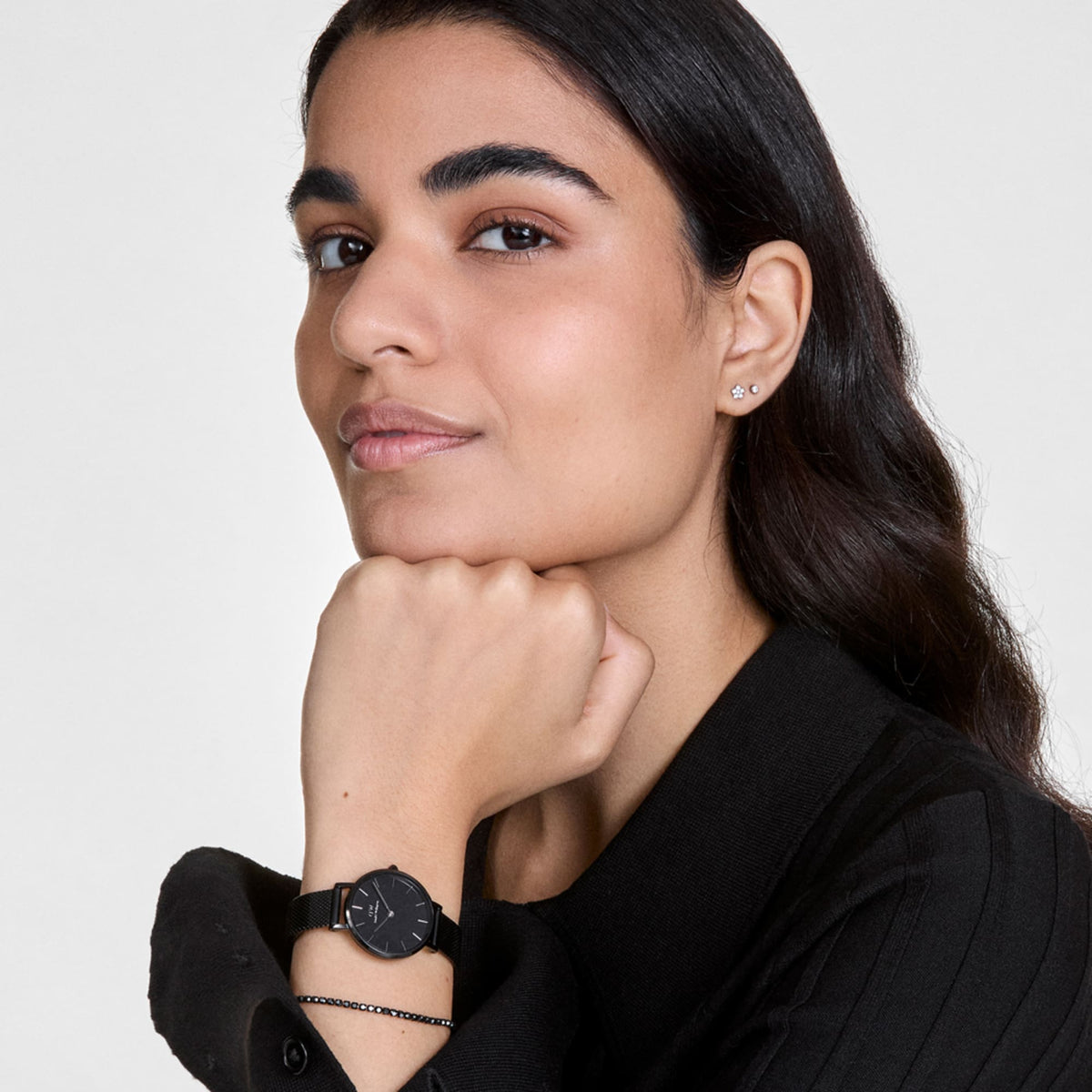 Woman wearing the Classic Tennis Bracelet Nightfall Rose Gold on her wrist, styled with a black watch and a black outfit, showcasing the delicate rose gold chain and midnight-toned crystals for a refined, modern look.