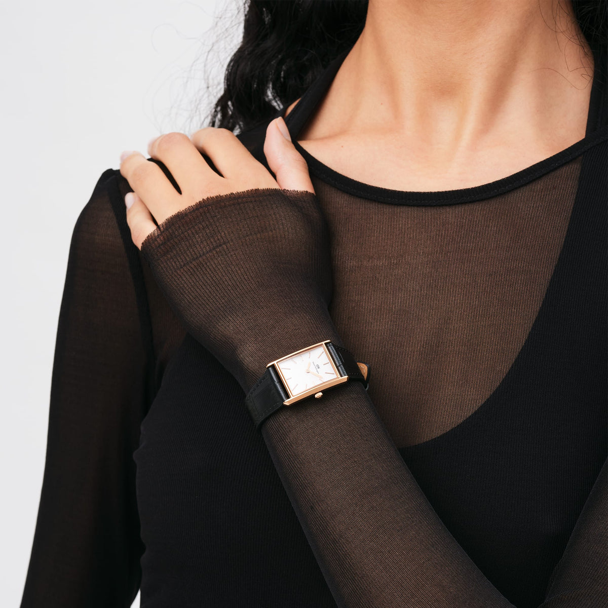 A woman wears the Bound Black Crocodile Rose Gold watch with a rectangular rose gold case and black crocodile-embossed leather strap, styled with a sheer black top.