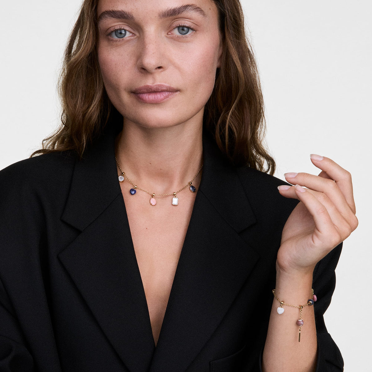 Woman wearing a gold charm necklace featuring a rose quartz oval gold charm alongside other colourful stones, paired with a matching gold bracelet for a coordinated, elegant look.