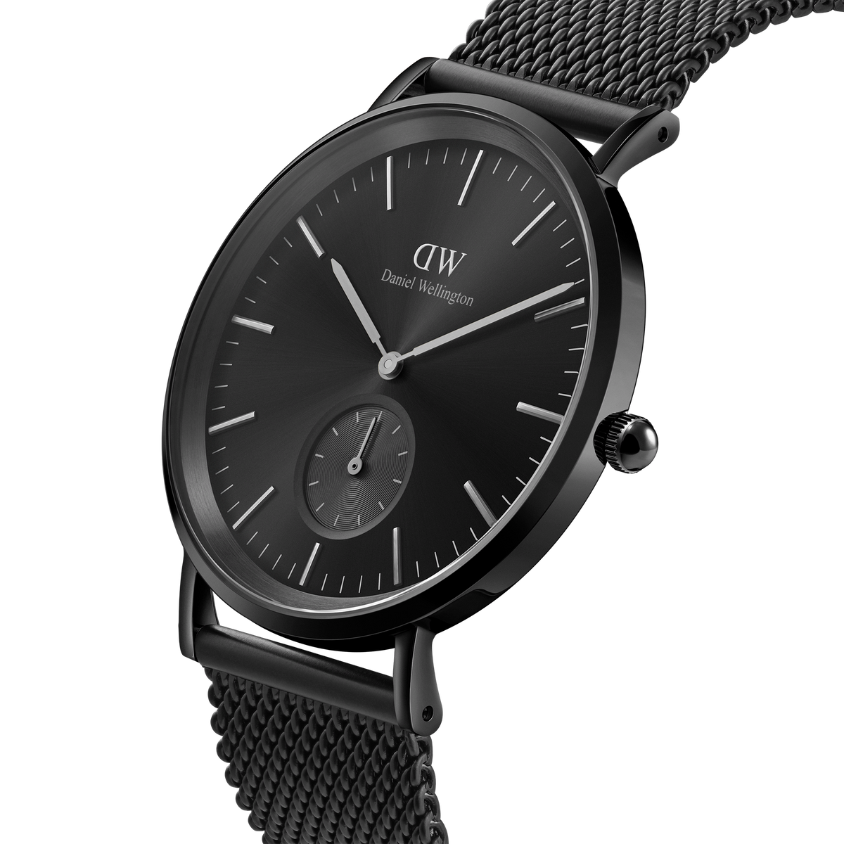 Classic Multi-Eye Ashfield Onyx watch with a black stainless steel mesh strap, minimalist black dial, and sub-dial for seconds, shown in a close-up angled view.