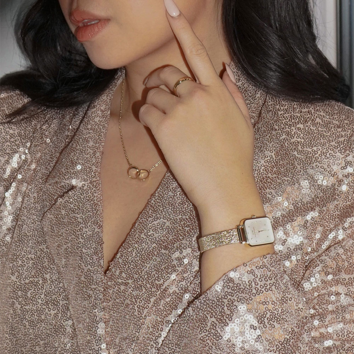 A woman wearing the Elan Unity Necklace Gold with interlocking rings, styled with a gold watch and sequin blouse for an elegant, coordinated look.
