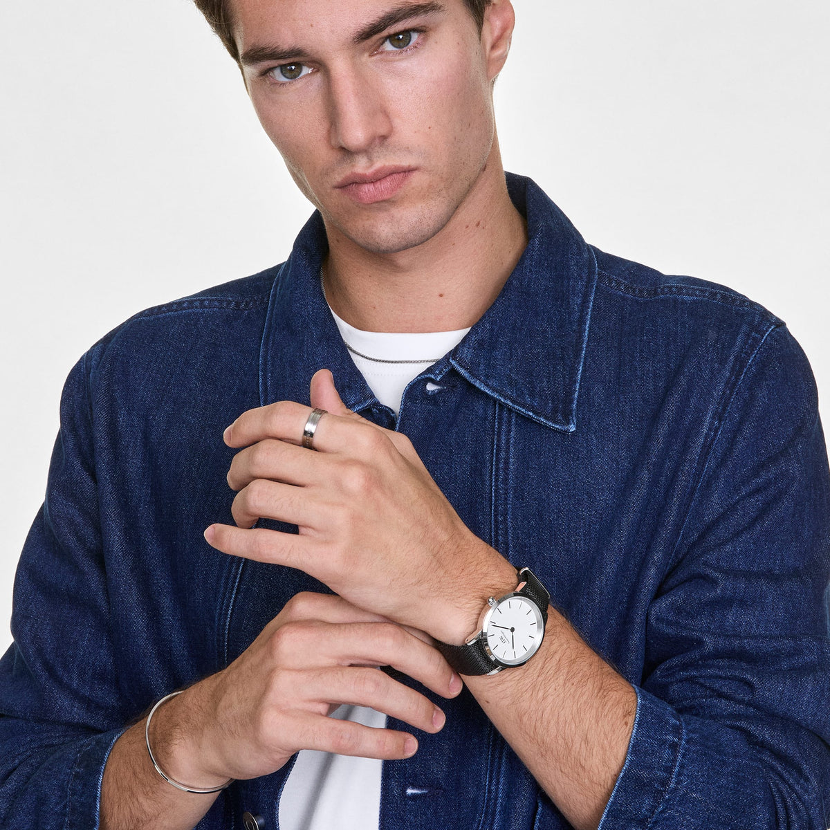 A man wearing the Elan Ring Silver on his finger, styled with a denim jacket, white t-shirt, and a classic Daniel Wellington watch for a modern, understated look.