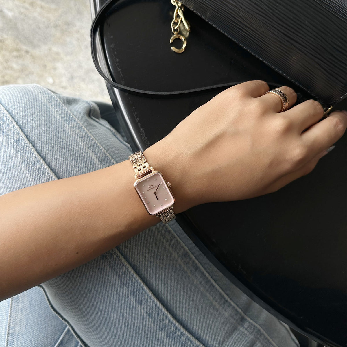 Woman wearing the Quadro Lumine 5 Link Melrose Pink MoP Rose Gold watch with a rectangular pink mother of pearl dial and rose gold bracelet, styled with casual denim and a black handbag.