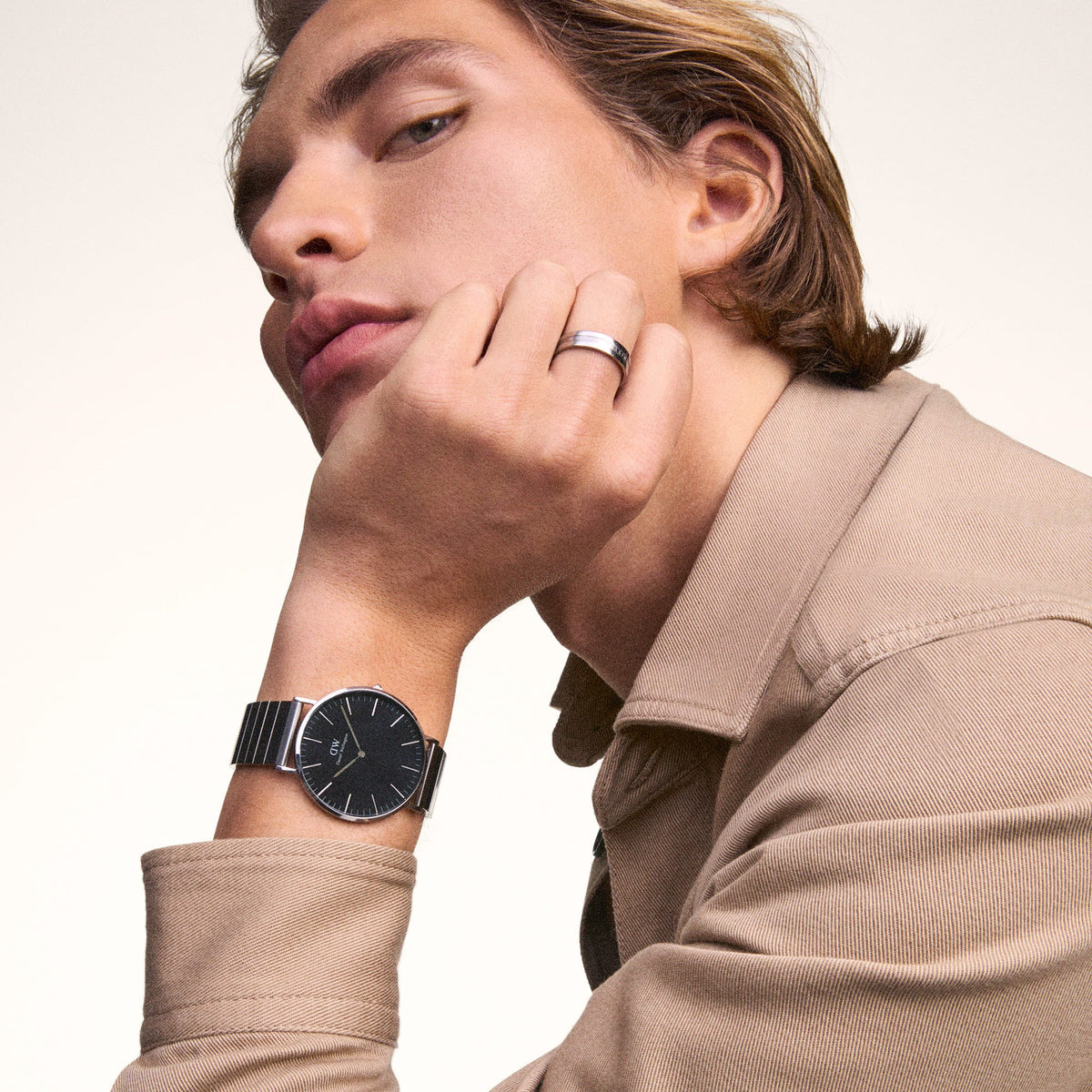 Man wearing the Classic Piano Link Onyx Silver watch by Daniel Wellington, featuring a brushed black dial and silver piano link strap, styled with a beige shirt for a refined, modern look.