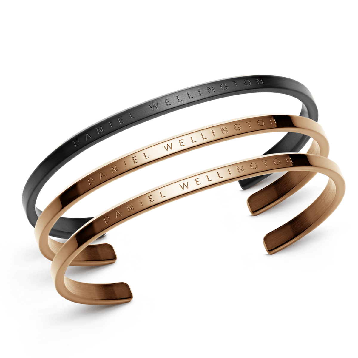 Three Daniel Wellington cuff bracelets are displayed, featuring one in sleek black and two in polished rose gold, each engraved with the brand’s signature for a refined, minimalist look. The set highlights a modern yet timeless style, ideal for stacking or wearing individually.