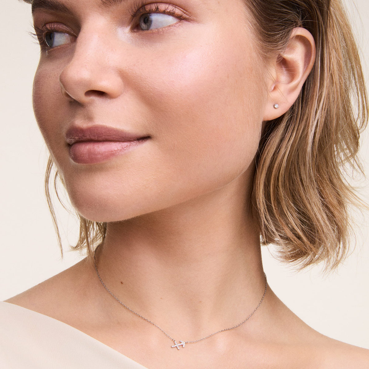 A woman wears the Crystal Stud Silver earring, a delicate cubic zirconia stud in a minimalist claw setting, styled with a fine silver necklace for an elegant everyday look.