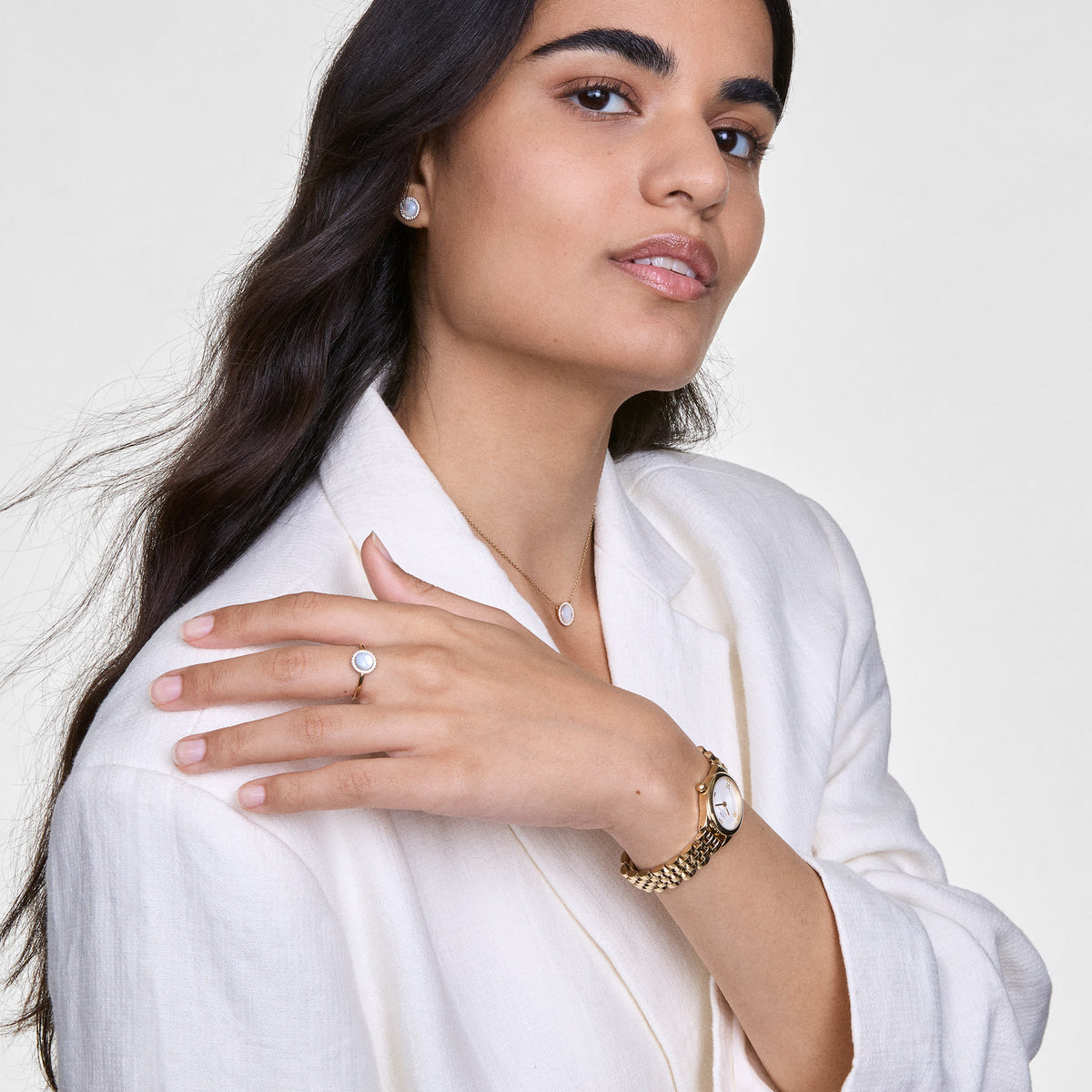 Woman wearing Audrey Earrings Mother of Pearl Gold, styled with matching mother of pearl jewellery and a gold watch, showcasing the elegant stud earrings against a cream blazer.