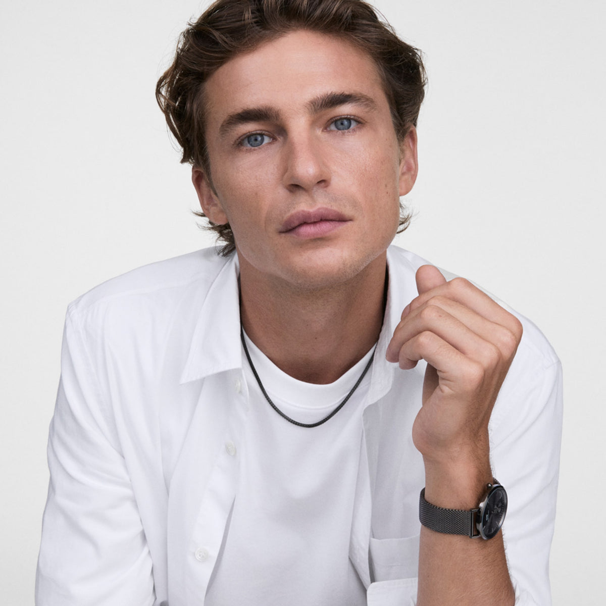 A person wears the Tide Mesh Necklace Graphite 1.8, a slim graphite mesh chain, styled with a white shirt and matching graphite watch for a modern, minimalist look.