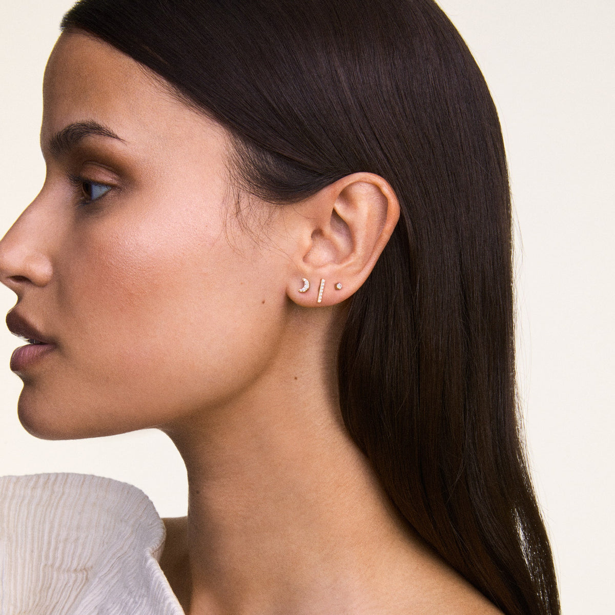 A woman wears the Crystal Moon Stud Gold earring, styled in a delicate crescent moon shape with sparkling cubic zirconia crystals, stacked with other minimalist gold earrings.