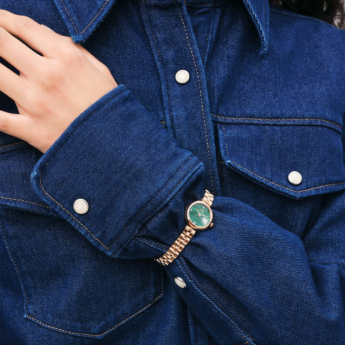 A woman wears the Elan Lumine Malachite Rose Gold watch with a green malachite dial and rose gold bracelet, styled with a dark denim shirt.