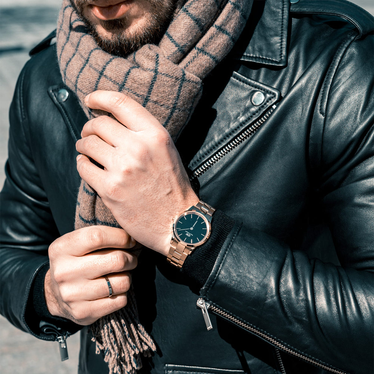 Man wearing Iconic Link Rose Gold watch with black dial, styled with a leather jacket and checked scarf for a modern look.