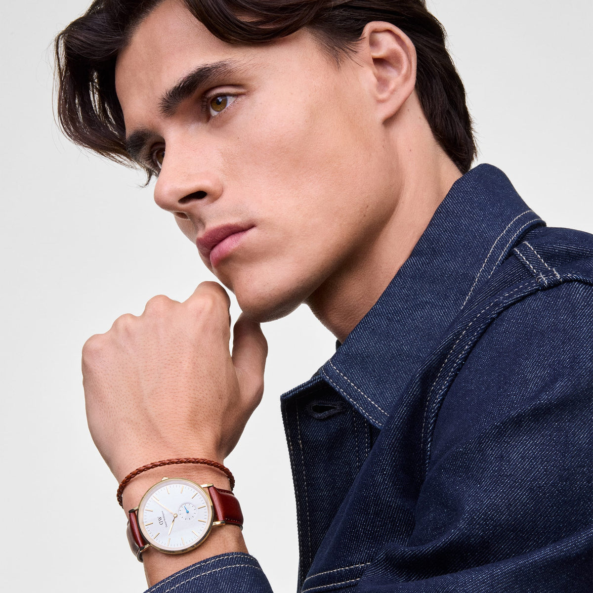 Man wearing the Daniel Braided Leather Bracelet St Mawes 2.8 Gold, styled alongside a classic watch with a brown leather strap, highlighting the slim braided brown leather band and polished gold clasp for a refined, layered look.