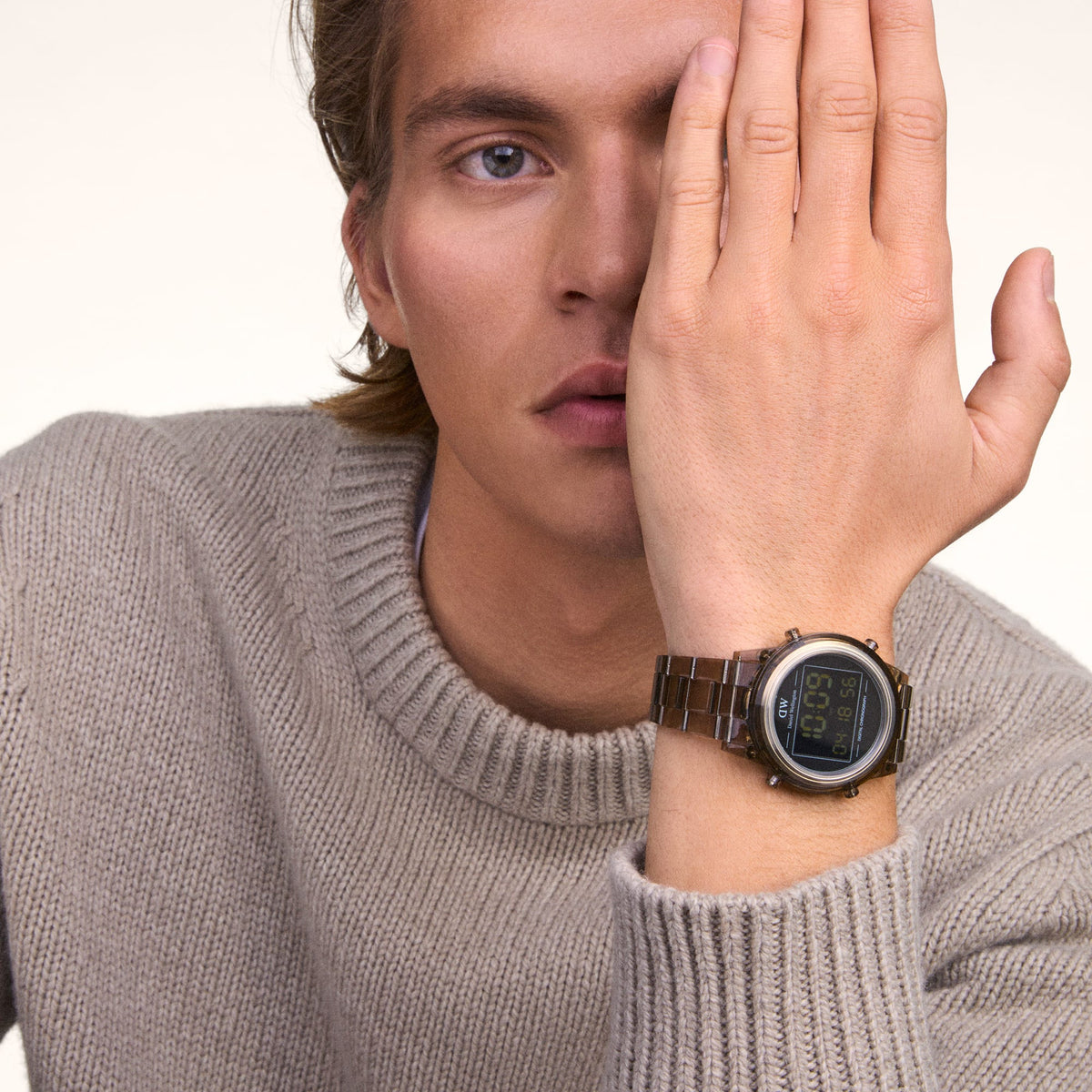 A man wearing the Daniel Wellington Retro Digital Dark Brown watch with a transparent brown bio-based plastic case and matching link strap, styled with a beige knitted jumper.