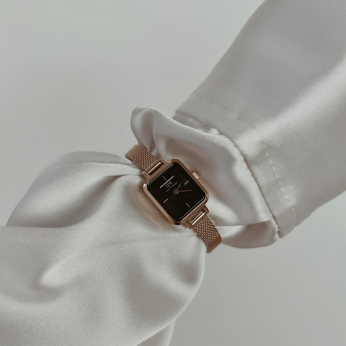 Quadro Mini Melrose Onyx women’s watch with a rectangular black dial and rose gold mesh strap, styled on a wrist with an elegant white blouse.