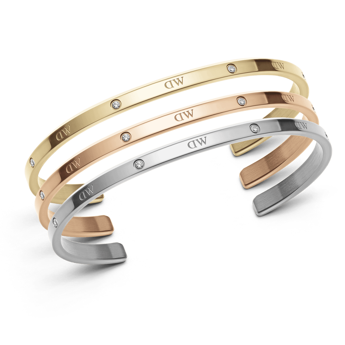 Set of three slim cuff bracelets in polished gold, rose gold, and silver finishes, each featuring subtle crystal accents and the engraved DW signature, displayed stacked together.