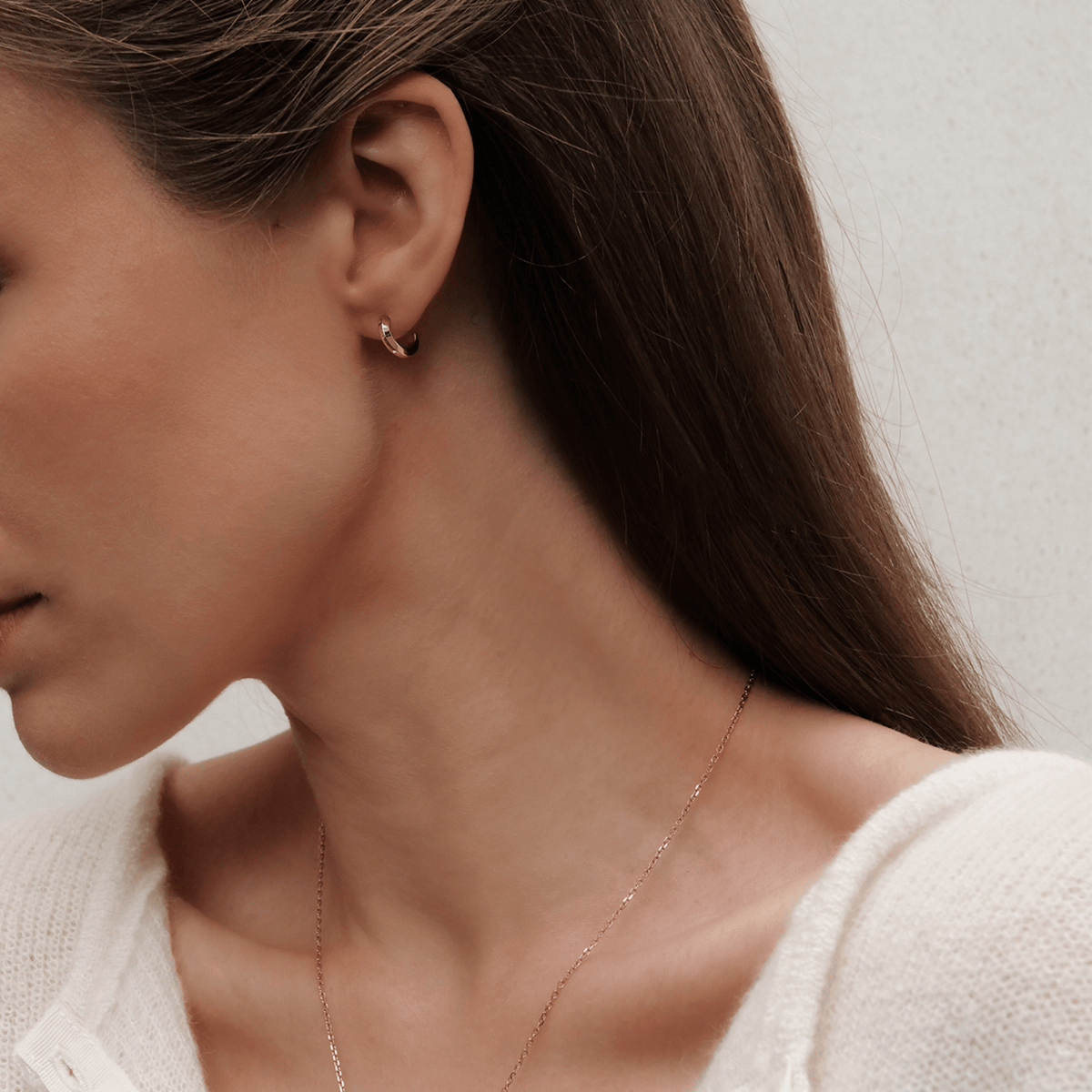 A woman wears a petite rose gold Elan earring with a curved, minimalist design and subtle engraved detailing, styled elegantly for everyday wear.