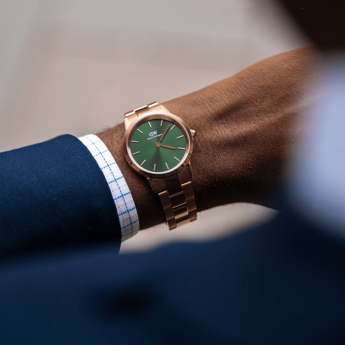The Iconic Link Emerald Green Rose Gold watch with a polished rose gold bracelet and emerald green dial, styled on the wrist with a blue suit jacket and checked shirt.
