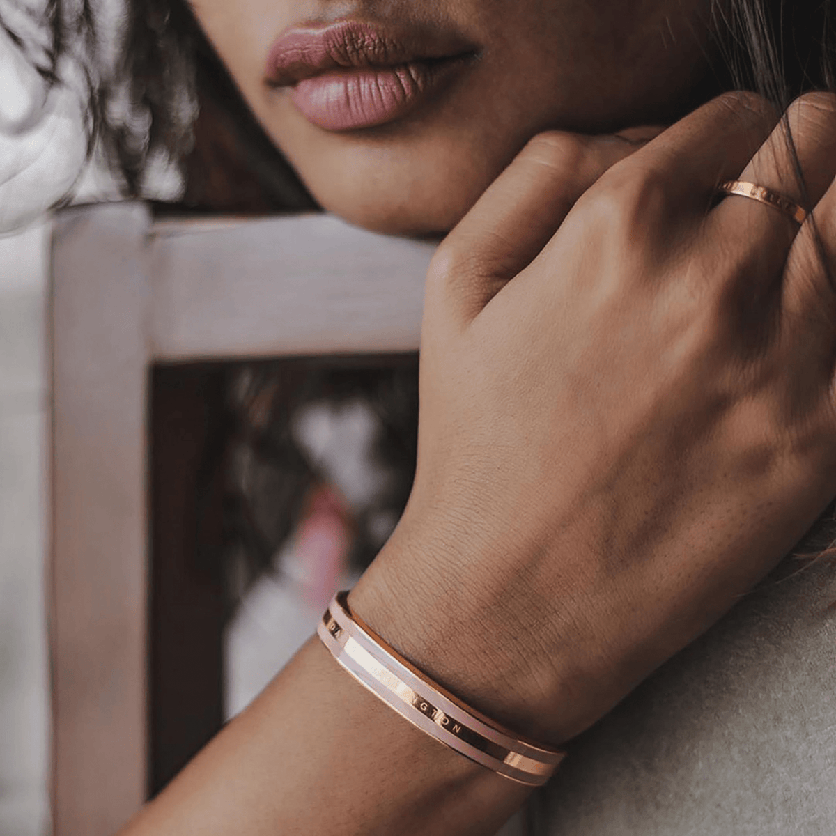 A woman wears the Daniel Wellington Emalie Bracelet in dusty rose and rose gold, showcasing its wide enamel inlay and engraved logo on her wrist.