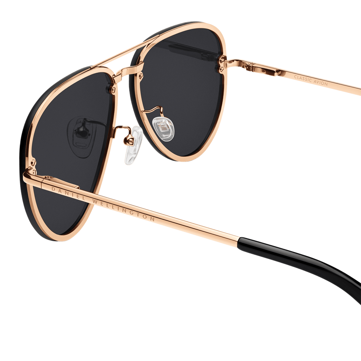 Close-up of Avion Steel Rose Gold sunglasses highlighting the rose gold stainless steel frame, black lenses, adjustable silicone nose pads, and engraved Daniel Wellington branding on the arm.