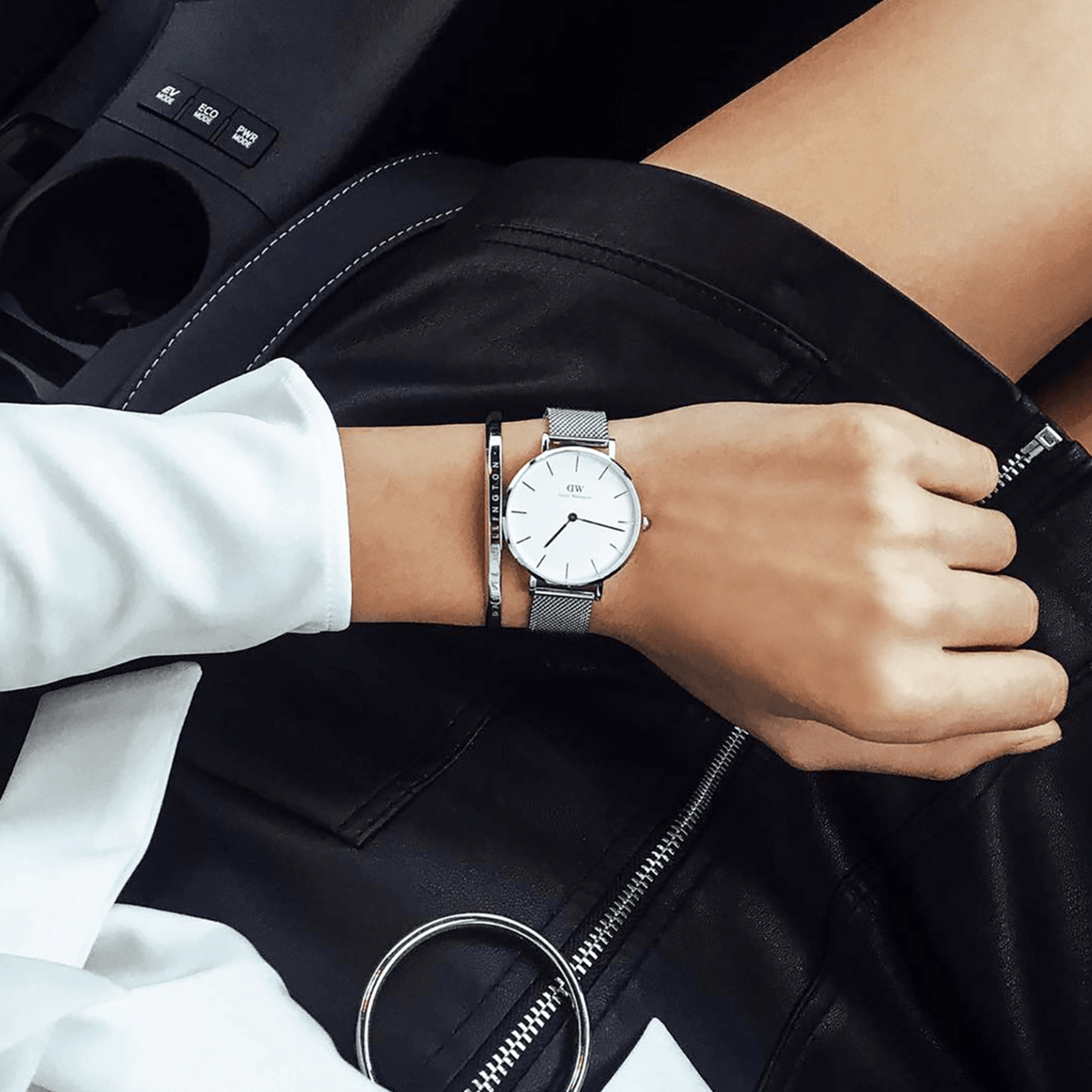 Petite Sterling silver mesh women’s watch with white dial, styled with a bangle and black leather skirt in a car setting.