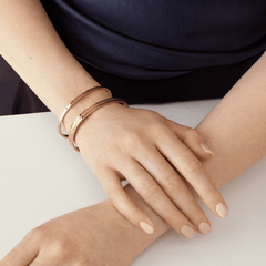 Two Daniel Wellington Elan Bracelets in rose gold, featuring an open cuff design and engraved logo, elegantly stacked on a woman's wrist.