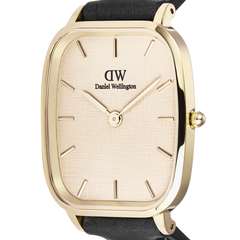 Close-up of the Marlon Sheffield Linen Gold watch by Daniel Wellington, showcasing its gold cushion-shaped case, linen-embossed dial, minimalist gold hour markers, and part of the black leather strap.
