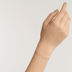 A delicate rose gold flat chain bracelet is worn on the wrist, showcasing its slim and minimalist design.